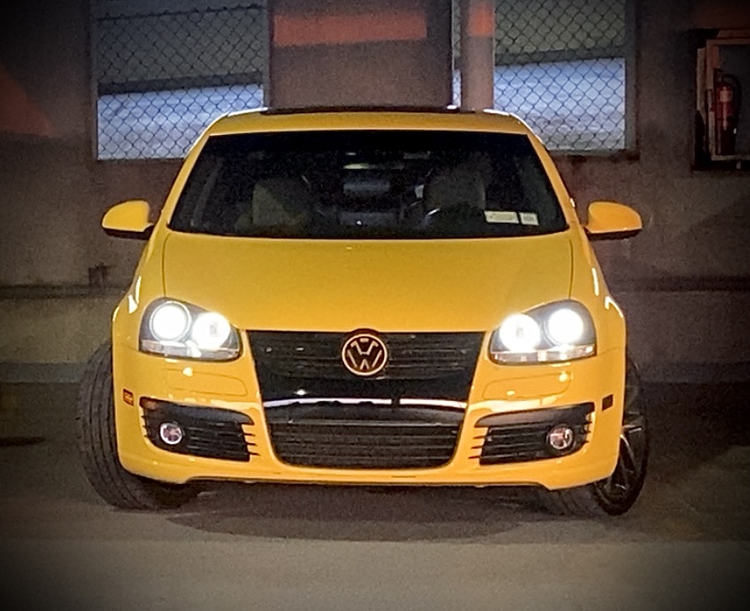 Front of Abby's yellow Volkswagen GLI with headlights on